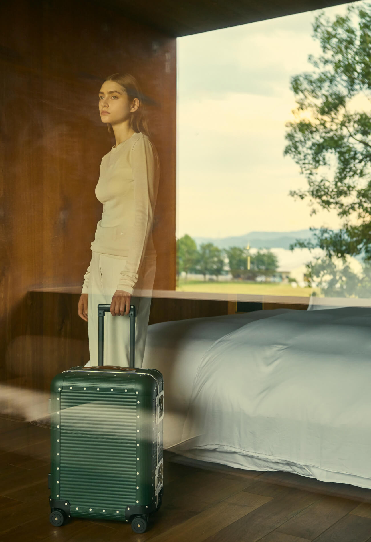 客室の窓辺に立つモデルと FPM のスーツケース